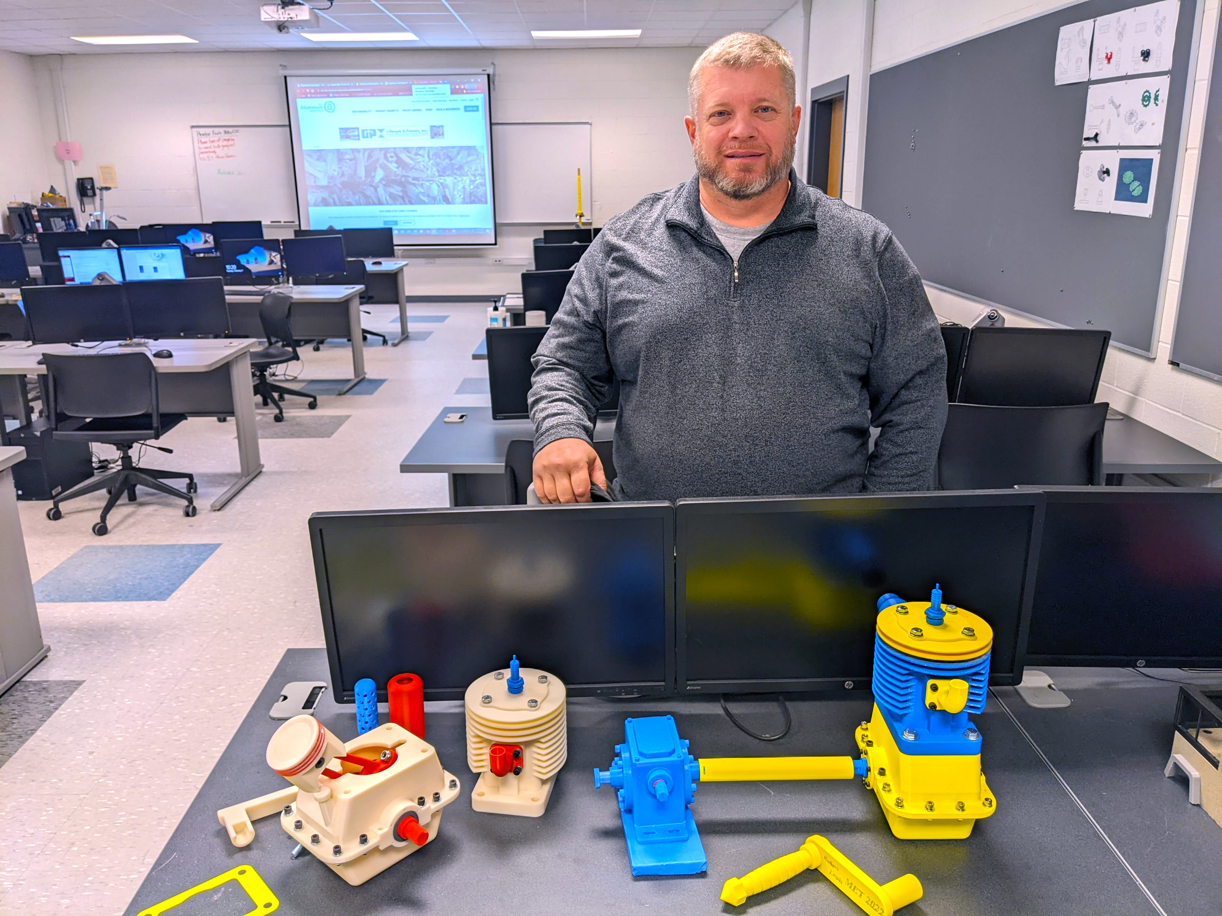 Student Robert Lewis stands with the two projects he created using SolidWorks.