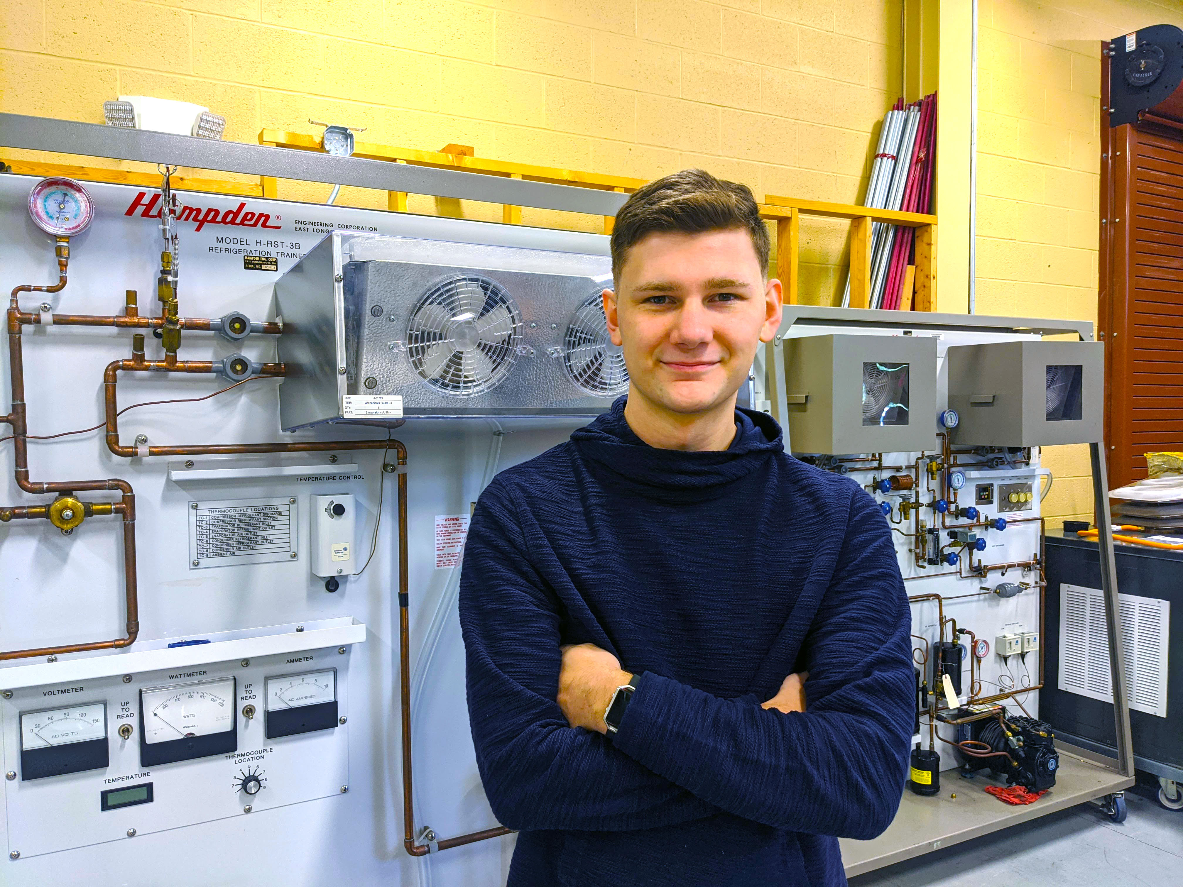 Sam Miles stands in front of a heating and air unit in the HVACR classroom.