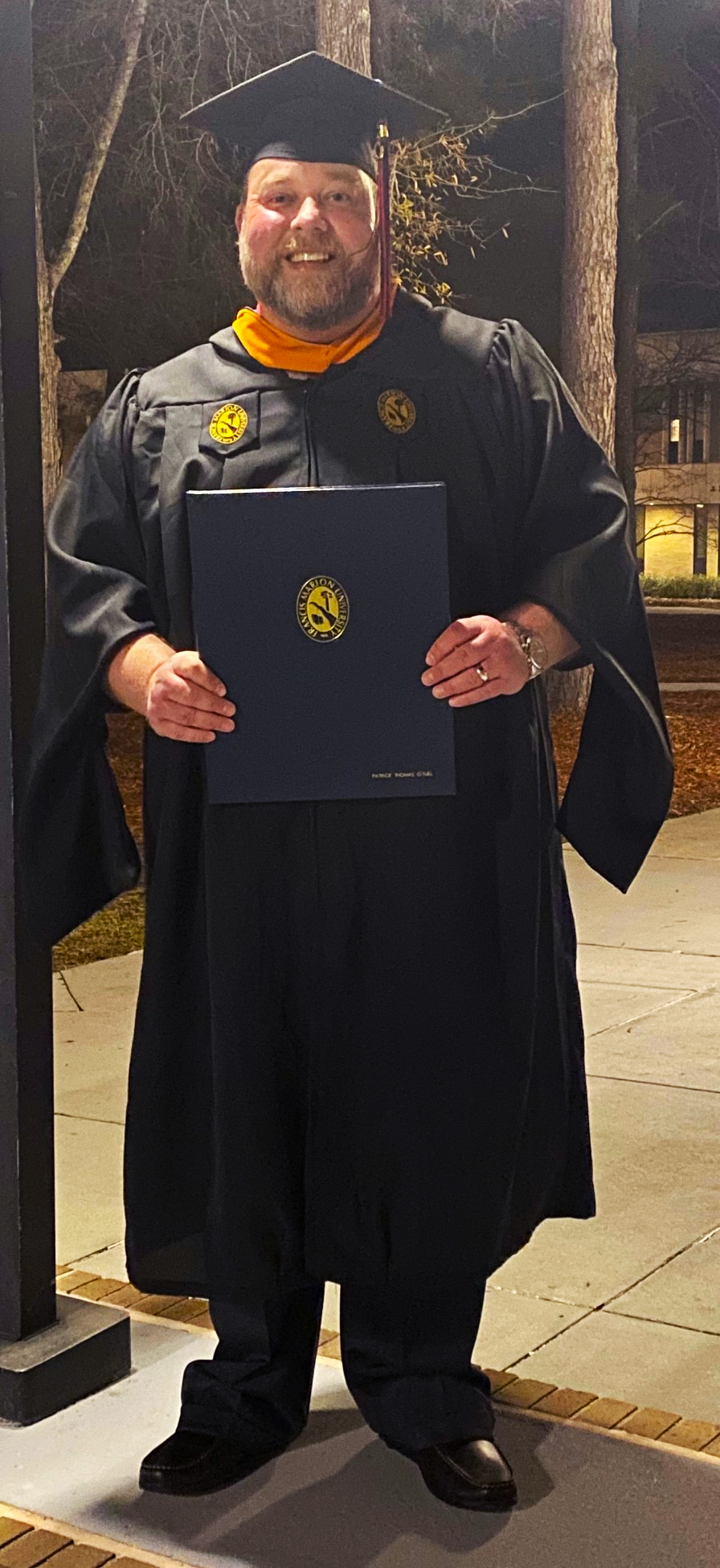Patrick O'Tuel in a cap and gown holding diploma