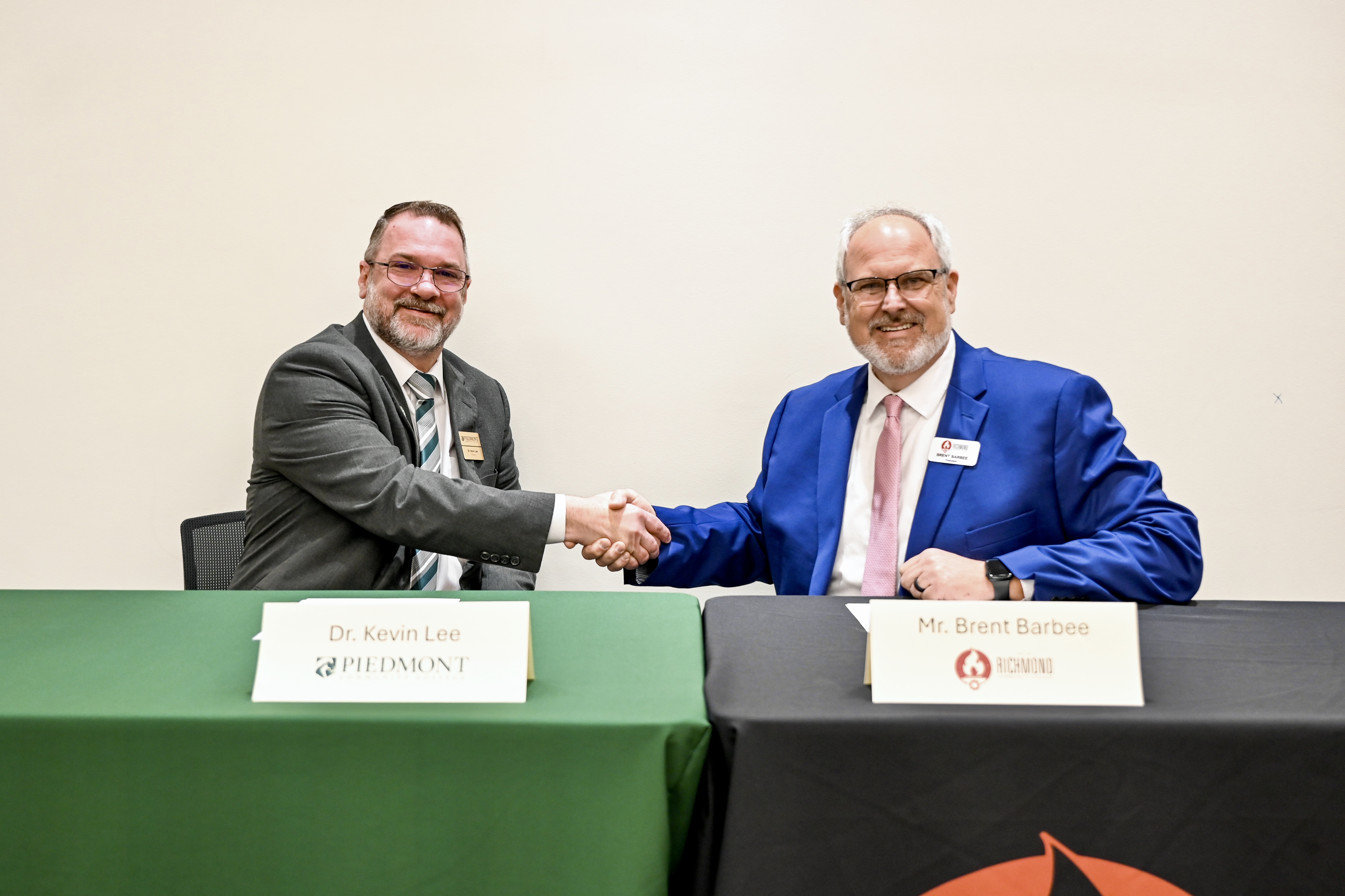 Community college presidents shake hands sitting at a table.