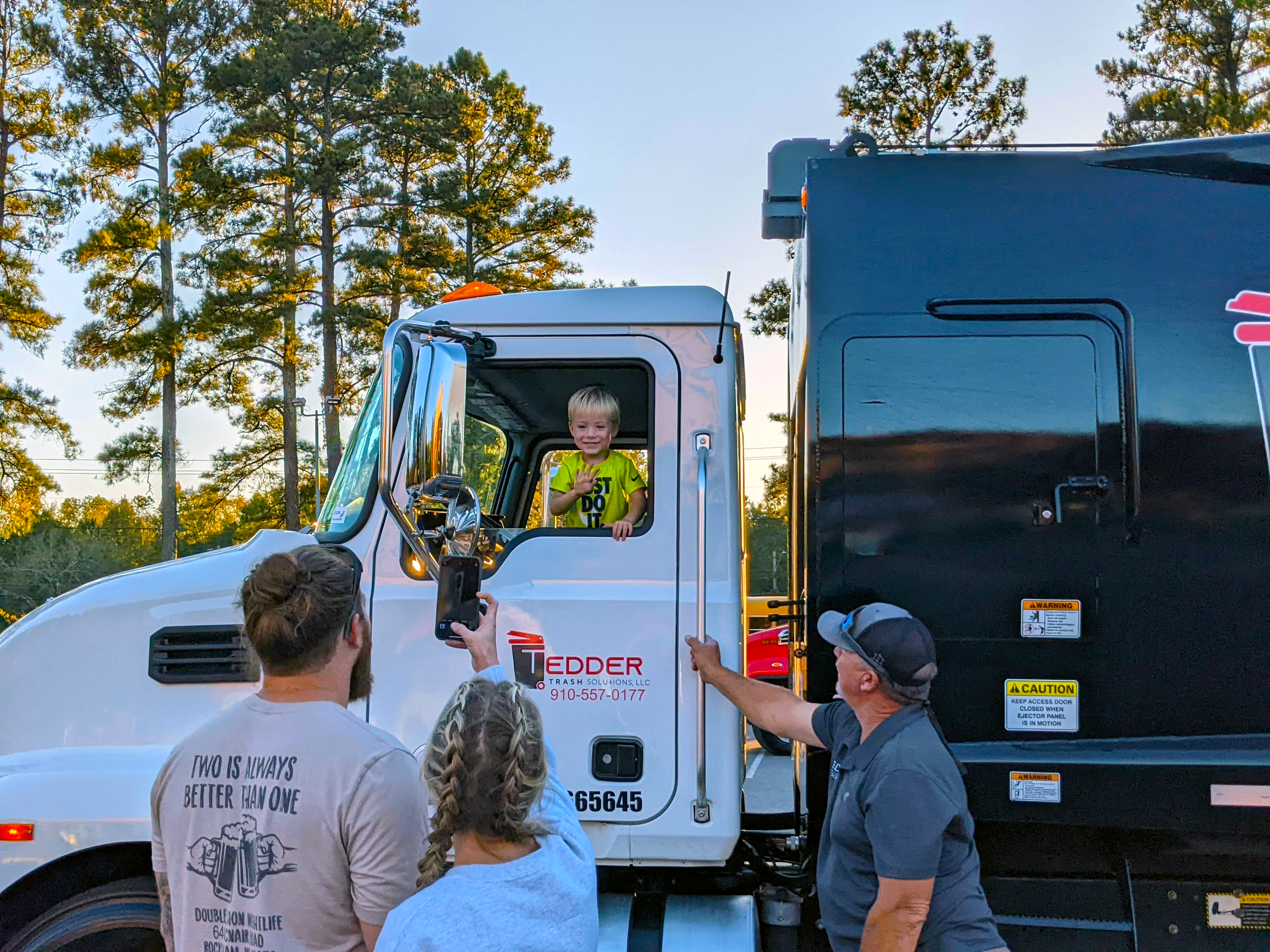 A child waves from the driver seat of a trash truck