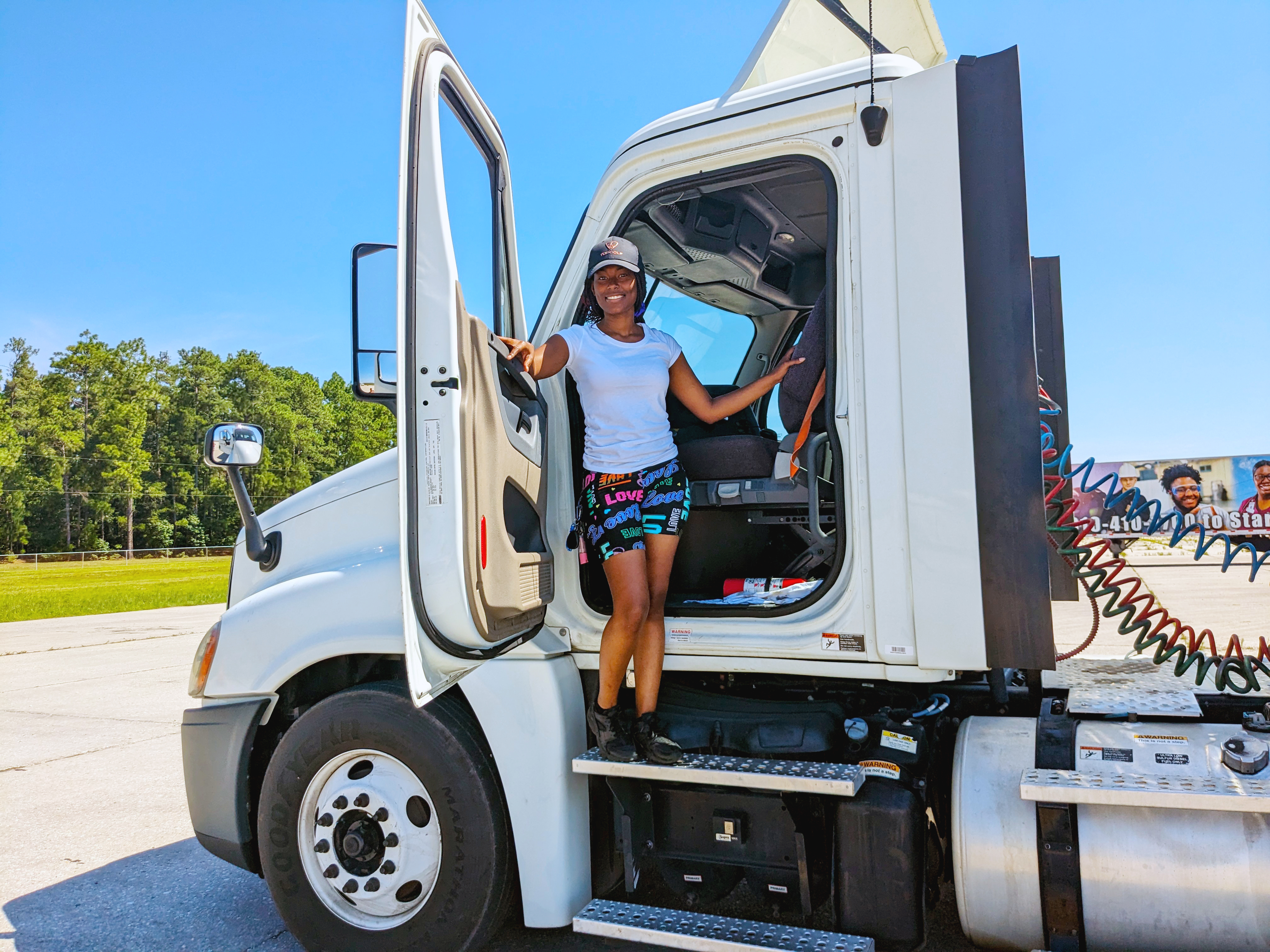 Female truck driver student stands in the cab of an 18-wheeler.