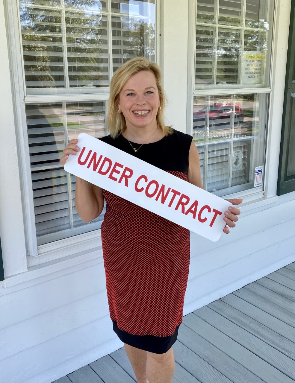 Alicia Krout holds a sign that reads "Under Contract" in front of a house