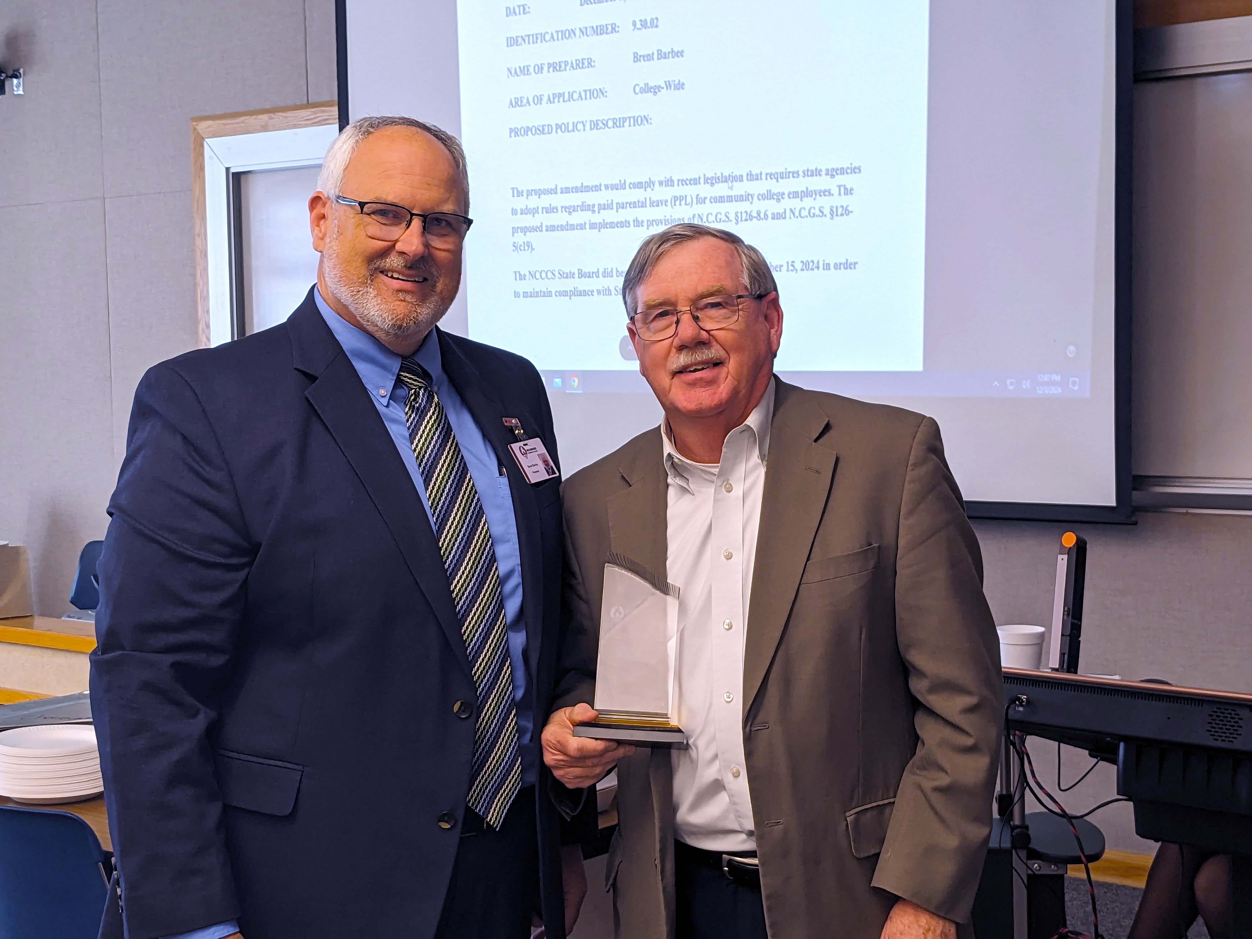 President Brent Barbee hands Trustee Lee Wallace an award.