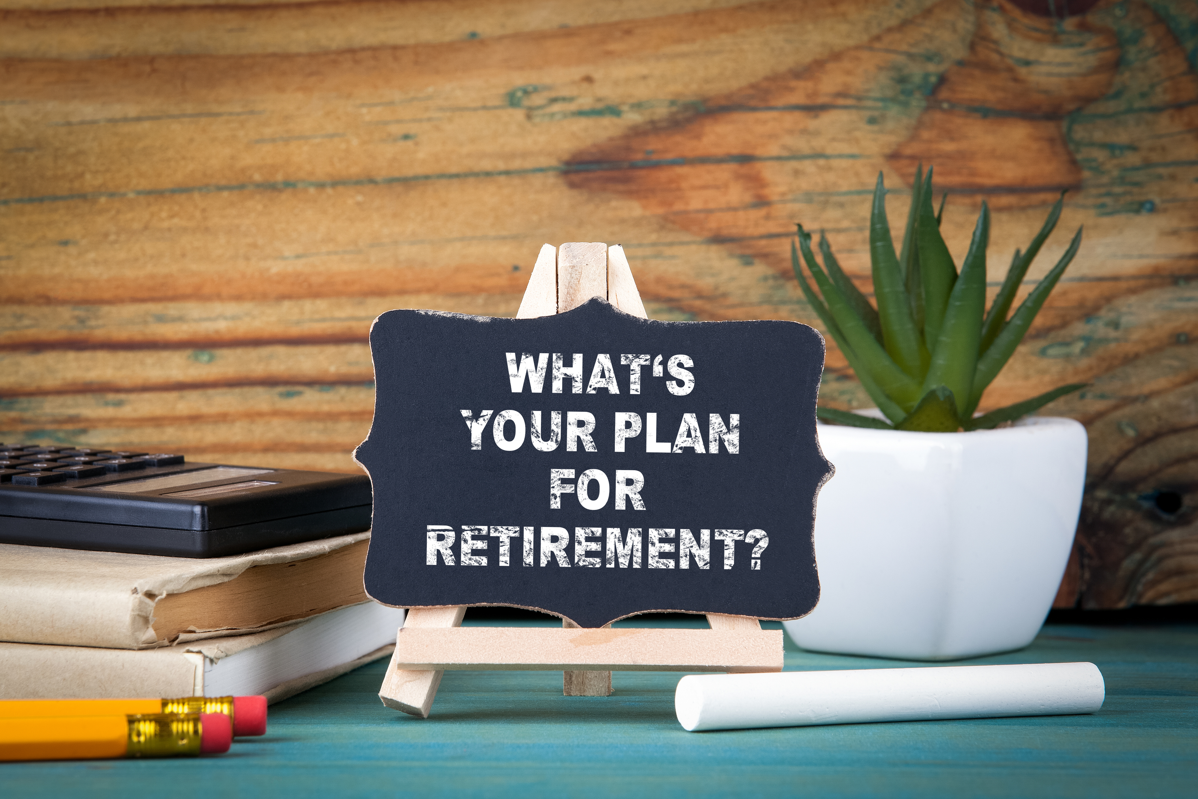 A small chalk board on a desk beside a plant and books. The chalkboard reads "What is your plan for retirement?"