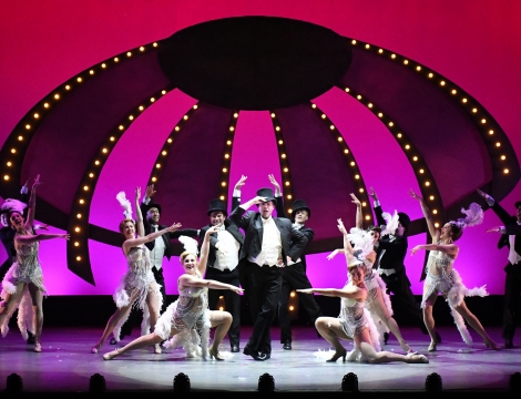 Singers and dancers on stage with a pink circus top in the background