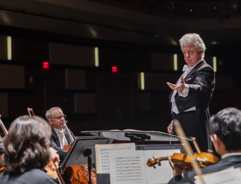 Photo of conductor of the Charlotte Symphony standing before string instrument players