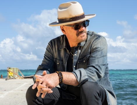 Phil Vassar sitting near the ocean with a hat and sunglasses