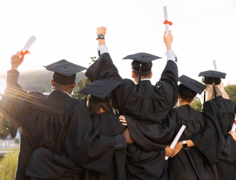 Photo of students graduating, holding up diplomas. Photo is taken from the back