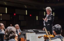 Photo of conductor of the Charlotte Symphony standing before string instrument players