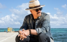 Phil Vassar sitting near the ocean with a hat and sunglasses