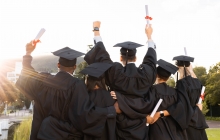 Photo of students graduating, holding up diplomas. Photo is taken from the back